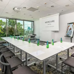 Sala konferencyjna w hotelu Mercure Poznań Centrum. Długi stół, krzesła, projektor i logo hotelu.
