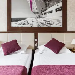 Dwie wygodne łóżka w pokoju hotelowym, nad nimi obraz z żaglówką. Idealne miejsce na wypoczynek, jak sugerują primavera jastrzębia góra opinie.