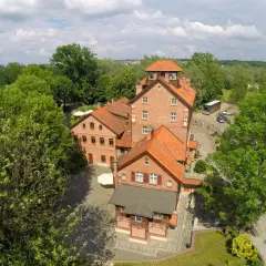 Hotel Młyn Elbląg, ceglane budynki z czerwonymi dachami, otoczone zielenią.