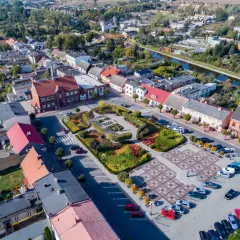 Widok z lotu ptaka na rynek w Barcinie, z kolorowymi rabatami kwiatowymi i brukowanym placem.