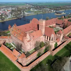 Malbork, największy zamek w Europie, rozciąga się wzdłuż rzeki. Potężne ceglane mury i czerwone dachy tworzą imponujący widok.