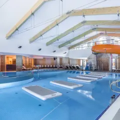 Wnętrze hotelu z aquaparkiem w górach. Basen z pomarańczowymi zjeżdżalniami, leżakami i dmuchanymi materacami.