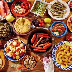 Obfity stół pełen hiszpańskich tapas: kiełbaski, krewetki, kalmary, owoce morza, ser, wędliny i tortilla.