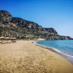 Piękna, piaszczysta plaża Tsambika z łagodnymi falami i skalistym wzgórzem w tle. Leżaki i parasole zapraszają do odpoczynku.