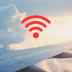Widok z okna samolotu na chmury i skrzydło. Czerwony symbol Wi-Fi unosi się w powietrzu, sugerując, czy w samolocie jest wifi.
