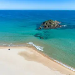 Pusta plaża na Costa Smeralda, z turkusową wodą i samotną postacią spacerującą brzegiem.