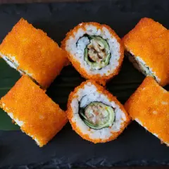 Roladki sushi California z pomarańczowym tobiko, ryżem, awokado i krewetką. Obok zielony listek i odrobina wasabi.