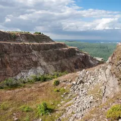 Widok na tarasową kopalnię kwarcu Stanisław. Skarpy skalne, kamienie i zieleń pod błękitnym niebem z chmurami.