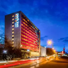 Wieczorna panorama miasta z oświetlonym budynkiem Park Inn Hotel Katowice i smugami świateł samochodów na drodze.