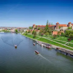 Widok na Wawel i Wisłę, najdłuższą rzekę w Polsce, z łodziami pływającymi po wodzie.