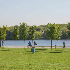 Spacer po zielonym brzegu zalewu nowohuckiego. Ludzie spacerują, jeżdżą na rowerze, ciesząc się słońcem i naturą.