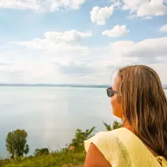 Kobieta w żółtej bluzce podziwia rozległe jezioro Balaton.