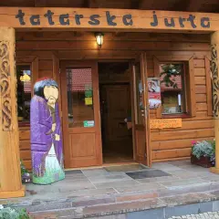 Drewniana fasada z napisem "tatarska jurta". Przed wejściem stoi kolorowa rzeźba postaci w stroju tatarskim.