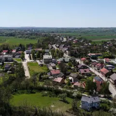 Widok z lotu ptaka na malowniczą wieś, która może pochwalić się mianem najmniejszego miasta w Polsce. Domy z czerwonymi dachami, kościół i zieleń pól tworzą sielski krajobraz.