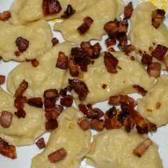 Pyszne pierogi galicyjskie posypane skwarkami z boczku, gotowe do zjedzenia. Obok leży widelec.