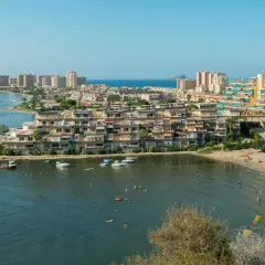 Widok na La Manga z plażą, budynkami mieszkalnymi i wodą pełną łodzi i kąpiących się ludzi.