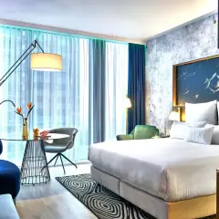 Nowoczesny pokój w hotelu NYX Warszawa: łóżko z białym pościelą, stolik kawowy, granatowe fotele i zielona sofa.