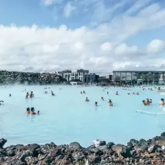 Ludzie kąpią się w turkusowej wodzie Blue Lagoon, otoczonej wulkanicznymi skałami i nowoczesnymi budynkami.