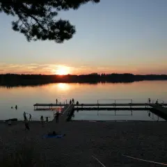 Zachód słońca nad jeziorem w Sompolnie. Ludzie odpoczywają na plaży i spacerują po pomostach.