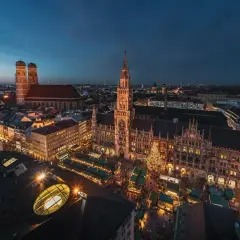 Nocny jarmark bożonarodzeniowy w Monachium. Rynek z oświetlonymi straganami i choinką, w tle majestatyczny Nowy Ratusz i katedra Frauenkirche.
