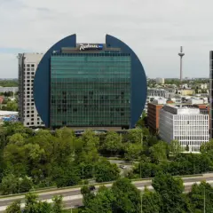 Charakterystyczny budynek Radisson Blu we Frankfurcie, otoczony zielenią, obok nowoczesnych wieżowców.