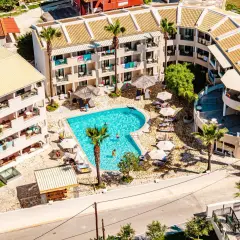 Widok z lotu ptaka na basen i budynki hotelowe. Wiele osób odpoczywa przy basenie. Warto sprawdzić caretta island hotel opinie przed rezerwacją.