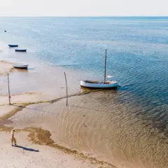 Spokojna plaża w Kuźnicy, gdzie kilka łodzi czeka na wodzie, a samotna postać spaceruje brzegiem.