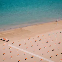 Pusta plaża w Rimini z rzędem pomarańczowych parasoli i małą łodzią. Woda jest turkusowa.