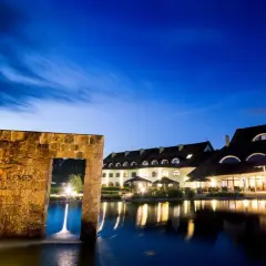 Hotel Remes Sport & Spa nocą, z kamiennym łukiem i stawem w tle.
