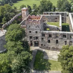 Ruiny zamku w Ząbkowicach Śląskich, z charakterystyczną okrągłą basteją i ceglanymi murami, otoczone zielenią.
