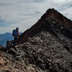 Alpinista na grani, zbliża się do najwyższego szczytu Gruzji. W tle pasmo górskie.