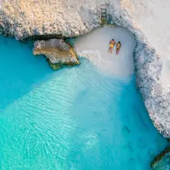 Para na plaży na wyspie Aruba, relaksująca się w turkusowej wodzie i na białym piasku, otoczona skalistymi klifami.