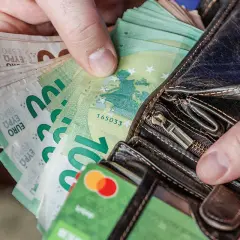 Ręce trzymają portfel z banknotami euro. Widać też kartę debetową. Litwa używa euro jako swojej waluty.