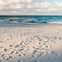 Piasek, fale i ślady stóp na plaży. Idealne miejsce, gdzie jechać nad morze na relaks.