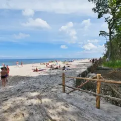 Słoneczna plaża w Karwieńskich Błotach pełna wypoczywających ludzi. Dzieci bawią się na piasku, dorośli opalają.