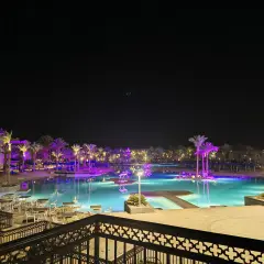 Nocny widok na basen z podświetlanymi palmami i budynkami hotelowymi. Albatros Palace Port Ghalib opinie potwierdzają jego urok.