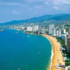 Słoneczna plaża w Acapulco z turkusową wodą, białymi hotelami i zielonymi wzgórzami w tle.