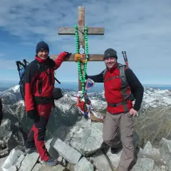 Dwóch turystów na szczycie w Tatrach Wysokich 2494 m, przy drewnianym krzyżu ozdobionym zielonymi paciorkami.