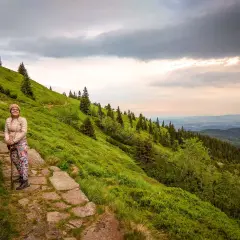 Kobieta na kamiennym szlaku w Dolinie Roztoki, otoczona zielonymi zboczami i lasem.