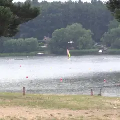 Pławniowice jezioro: wiatr napędza żaglówkę, a na brzegu widać piaszczystą plażę i drzewa.