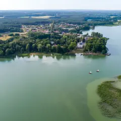 Malownicze jezioro Niesłysz z widokiem na wieś, lasy i dwa żaglówki na wodzie.