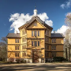 Żółty, wielopiętrowy budynek w stylu eklektycznym, przypominający pałac, otoczony drzewami. To malowniczy dworek Antonin.