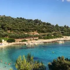 Słoneczna plaża na wyspie Vis, z turkusową wodą, zielonymi wzgórzami i ludźmi odpoczywającymi na piasku.