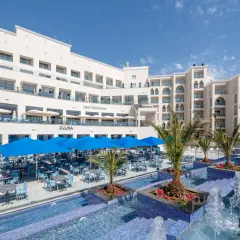 Luksusowy hotel z basenem i restauracją na świeżym powietrzu. Widać palmy, niebieskie parasole i stoły z krzesłami. Idealne miejsce na wakacje, jak na zdjęciach z **pickalbatros**.