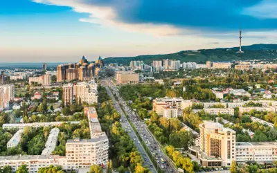 Widok na Almaty, dawną stolicę Kazachstanu, z wieżą telewizyjną w tle i ruchliwą autostradą pośród zieleni.