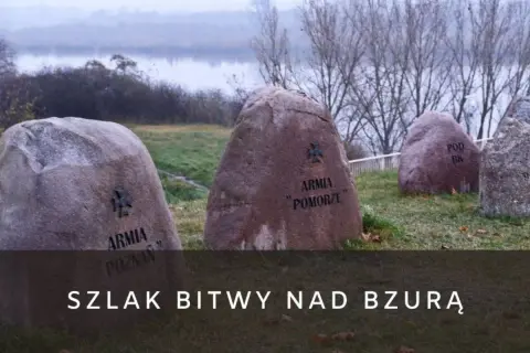 Kamienie pamięci z nazwami armii upamiętniają bitwę nad Bzurą. W tle rzeka i drzewa.
