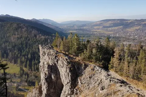 Widok z Nosala, góry samobójców, na Tatry i Zakopane. Skalisty szczyt, las i dolina.