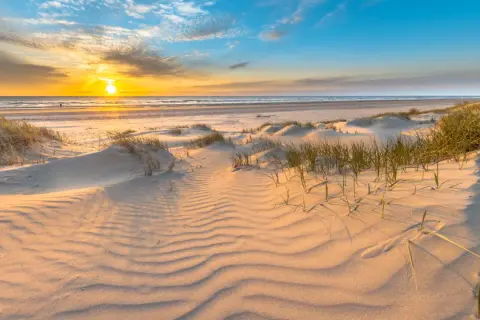 Piaskowe wydmy i trawy na plaży w Gdańsku o zachodzie słońca. Piękne morze i niebo.