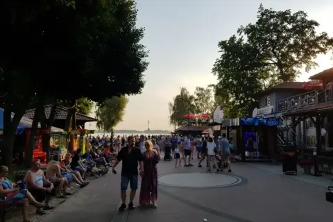 Skorzęcin atrakcje: tętniąca życiem promenada nad jeziorem, z ludźmi spacerującymi, siedzącymi na ławkach i korzystającymi z letnich rozrywek.