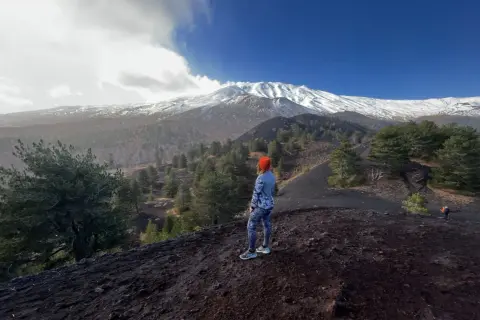 Kobieta w pomarańczowej czapce podziwia majestatyczny wulkan Etna pokryty śniegiem.